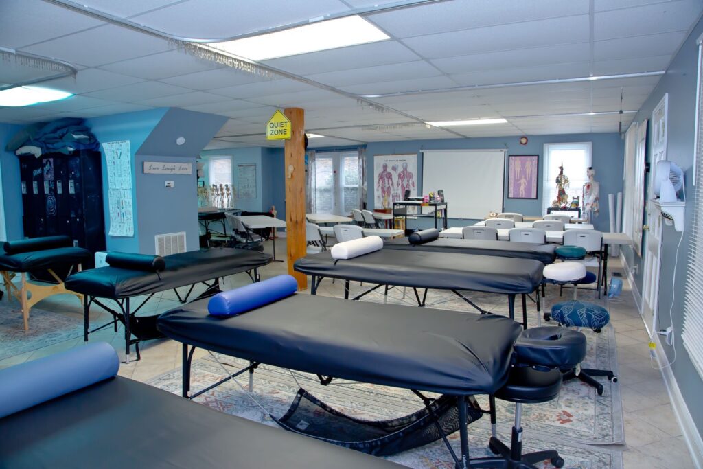 NC Massage School classroom with massage tables set up for hands-on practice, anatomy charts and skeleton models along the walls