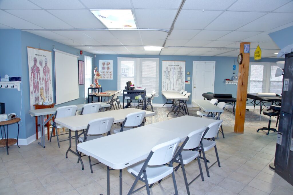 NC Massage School lecture classroom with tables and chairs, anatomy charts, and window light